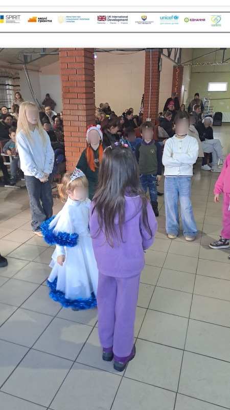 Дівчатка стоять у колі. На задньому плані  - сидять жінки, діти.