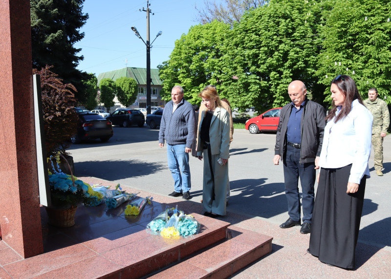 Представники влади стоять перед пам'ятним знаком загиблим захисникам і захисницям, схиливши голови, на підніжжі пам'ятного знака - квіти.