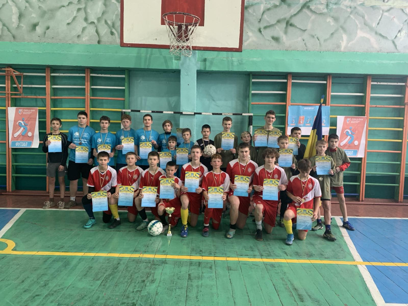 Спільне фото  переможців і призерів змагань. Діти тримають в руках грамоти, у кожного є медаль. Перед дітьми на підлозі стоїть кубок, лежить м'яч.                                                                                               