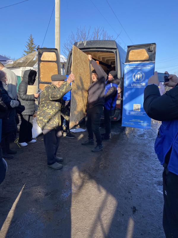 Представники "Проліски"  передають  із машини двом жителям громади  лист ОСБ плити.    