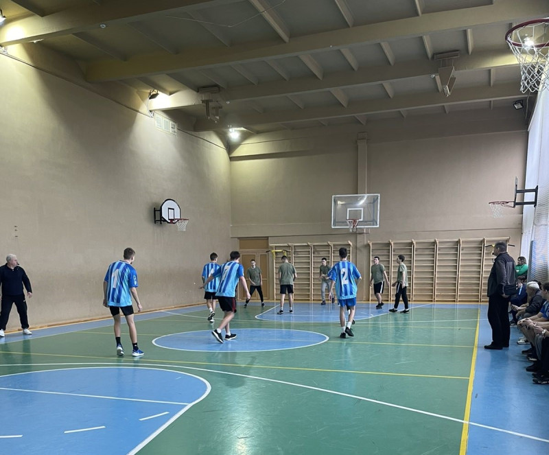 момент гри у спортивній залі, юнаки з двох команд біля баскетбольного кільця. Праворуч на лаві - представники ліцеїв.