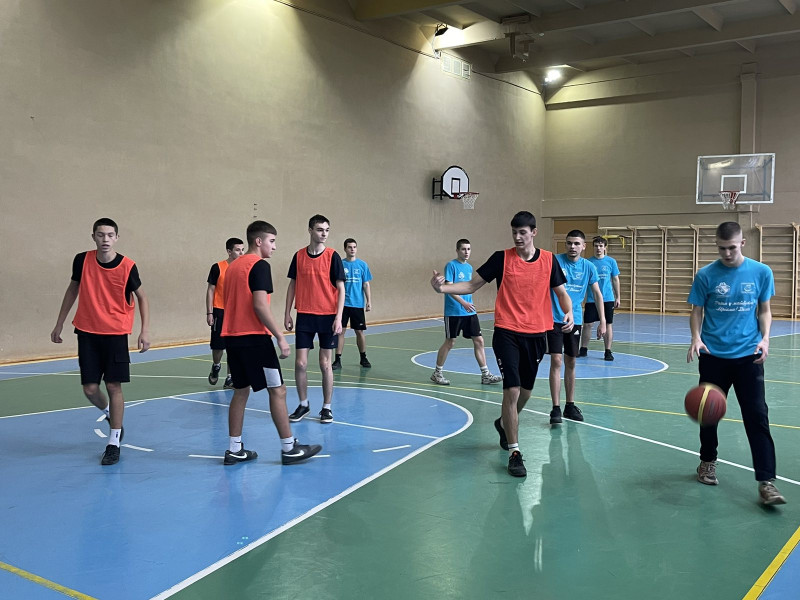 момент гри у спортивній залі: гравці з двох команд посередині зали, спілкуються. Один гравець із м'ячем в руках. 