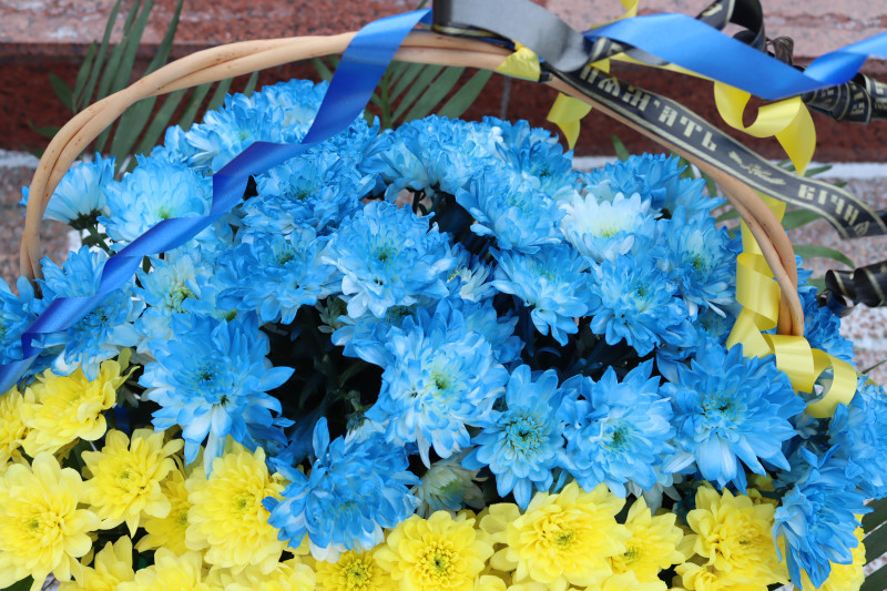 Кошик із синіми та жовтими хризантемами, синьою, жовтою та чорною стрічками.