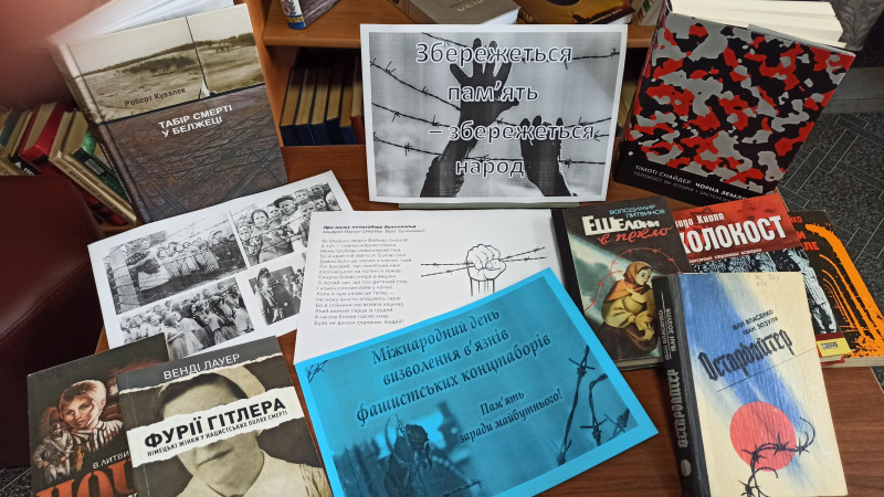На столі лежать різні книги, листівки з написами: " Міжнародний день визволення в'язнів фашистських концтаборів. Пам'ять заради майбутнього!" та " Збережеться пам'ять - збережеться народ!"