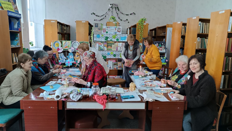 Учасниці заходу за роботою: сидять за столами, хтось стоїть. Спілкуються між собою, виготовляють свої вироби. 