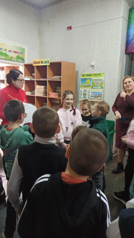 Діти у бібліотеці спілкуються з бібліотекарем. Поряд - класний керівник.