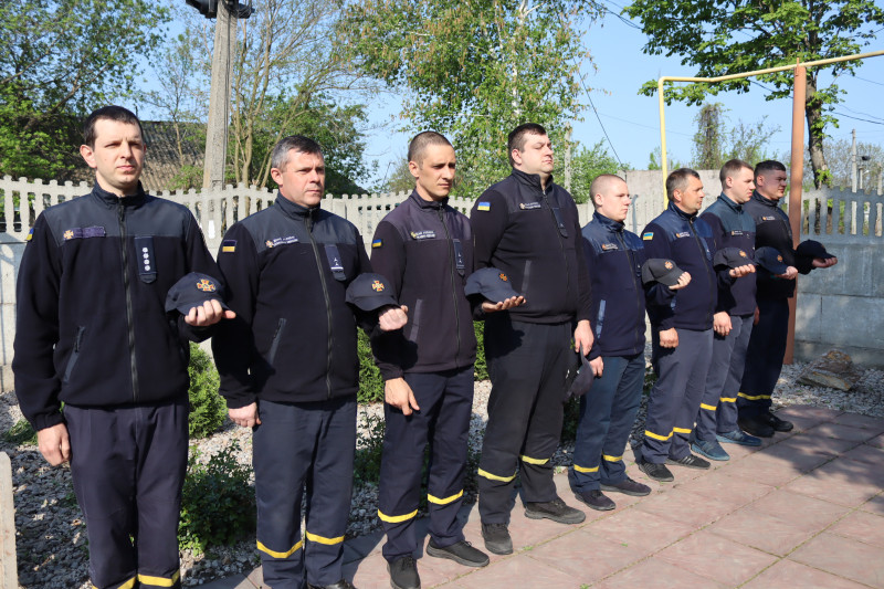 Хлопці - рятувальники стоять у хвилині мовчання, знявши головні убори.