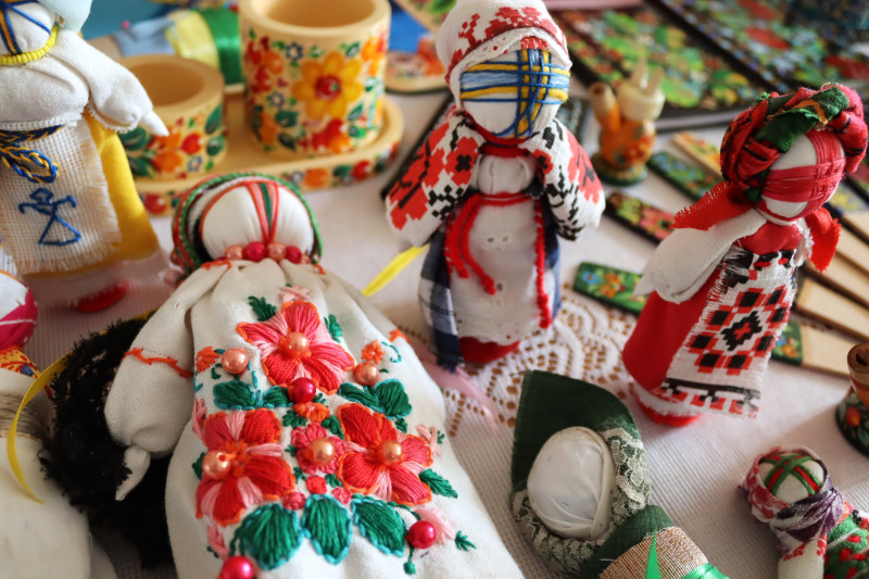 На столі лежать вироби: ляльки-мотанки, розписані петриківкою дерев'яні ложки, стаканчики.