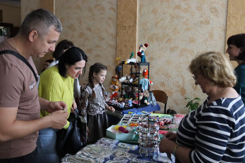 Чоловік, жінка та дитина роздивляються вироби, що лежать на столі. За столом стоять майстрині.