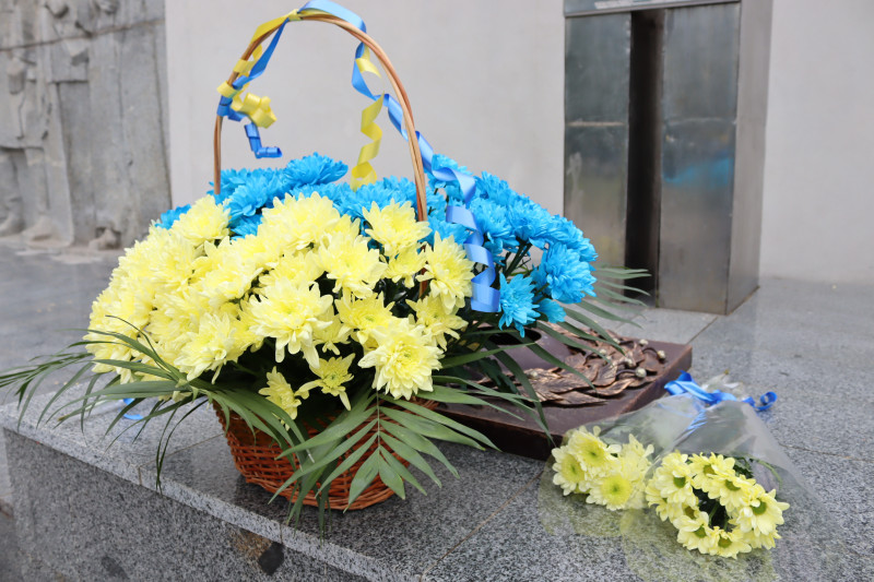 Кошик із синьо-жовтими хризантемати стоїть  біля стелли. Біля нього - букет із жовтими хризантемати.