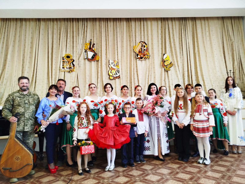 Спільне фото учасників концертної програми: діти, викладачі, директор школи, гість заходу - Захисник України Віталій Мороз із бандурою. Усі дівчата у вишиванках, викладачки з квітами в руках.