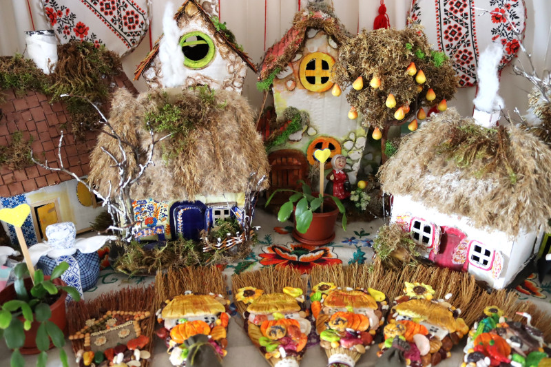 На столі - експозиція з виробів ручної роботи: українські хатки, обереги - вінички.  