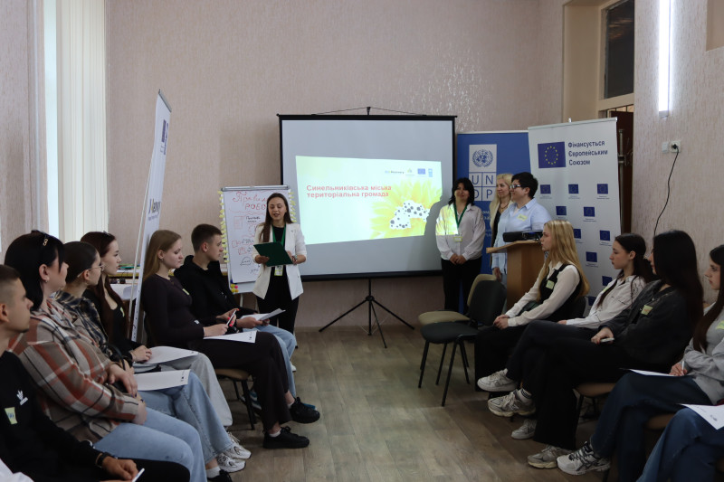 Під стіною - екран  із презентацією, праворуч і ліворуч - організаторки заходу. Вздовж зали - два ряди, сидять діти, погляди  - на екран та доповідачку. 