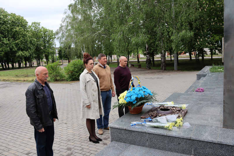 Представники міської та районної влади стоять перед меморіалом. Кошик  із квітами та букети лежать на підніжжі.  У хвилині мовчання вшановують пам'ять полеглих. 