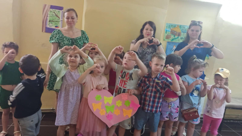 Усміхнені діти разом з дорослими показують сердця руками