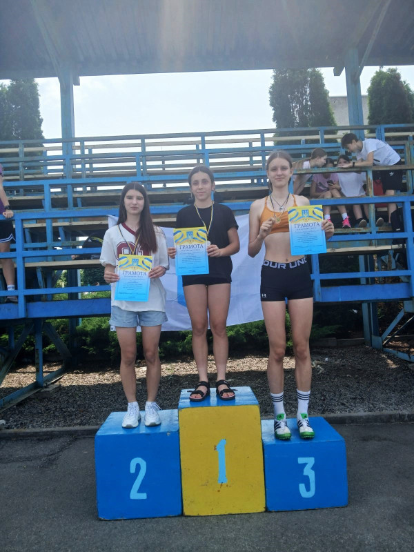 Троє дівчат стоять на п'єдесталі для нагородження з медалями і грамотами. 