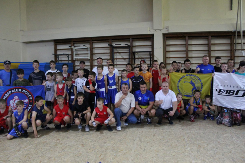 Спільне фото юних боксерів із тренерами у спортивній залі. Діти тримають у руках плакати із назвами клубів, федерацій. 
