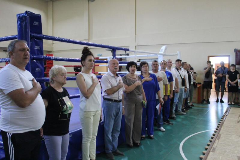 Представники влади, тренери стоять вздовж рингу, тримаючи праву руку на  серці. 