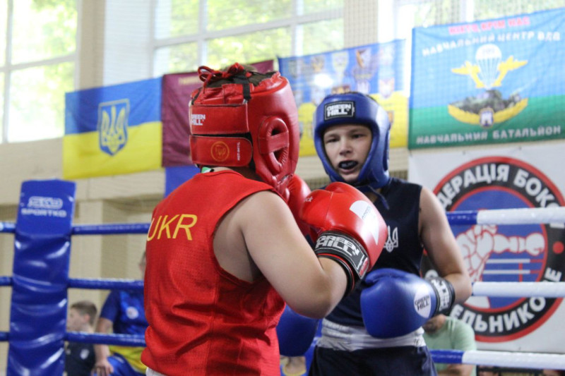 Момент двобою двох боксерів: один у червоній формі, інший - у темно-синій.  