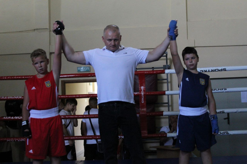 Максим Гончар на рингу підняв догори одночасно  руки двох юних спортсменів. Один хлопець - у червоній формі, другий - у темно-синій.