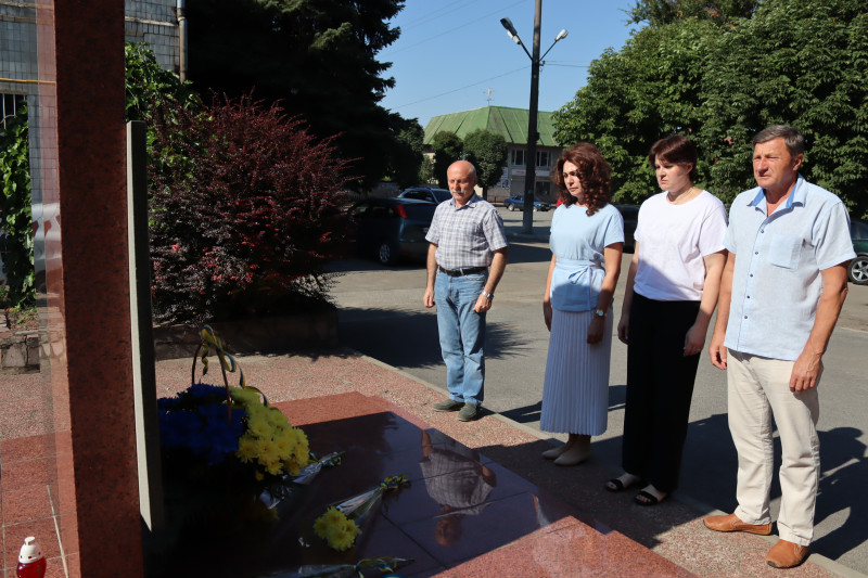Представники міської і районної влади стоять у підніжжя пам'ятного знака, схиливши голови у хвилині мовчання. У  підніжжя знака - квіти.