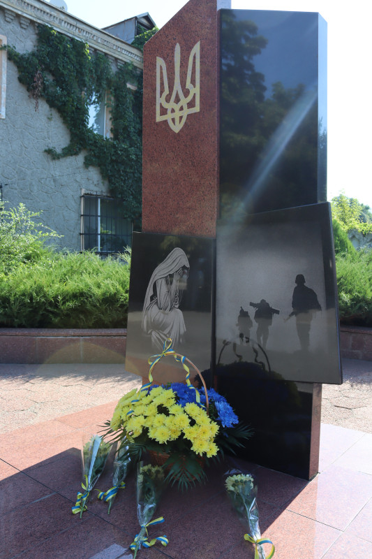 Пам'ятний знак на честь загиблих Героїв сучасності: стела з Гербом України вгорі та двома дошками. На одній - схилена у журбі мати, на іншій - силуети солдат, які йдуть удалечинь. У підніжжя - кошик із синьо-жовтими квітами, окремі букети.  