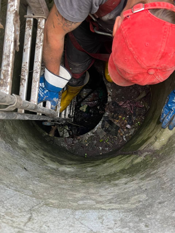 Працівник спускається у колодязь по драбині. На дні колодязю лежить сміття. 