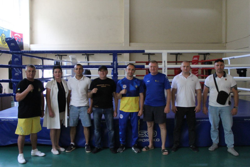 Спільне фото: вздовж рингу стоять чоловіки, вдягнені по-спортивному,  та одна жінка- медичний працівник.  