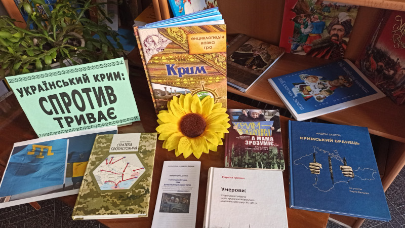 На столі - книги з тематикою :"Український Крим: спротив триває". У центрі стола - квітка соняшника. 