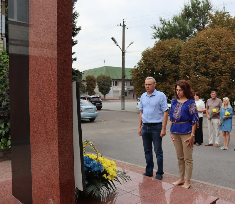 Міський голова Дмитро Зражевський, заступник голови Синельниківської районої військової адміністрації Тетяна Завалій, інші посадовці стоять перед пам'ятним знаком загиблим Героям, вшановують пам'ять у хвилині мовчання.  У підніжжя пам'ятного знаку - кошик із квітами.
