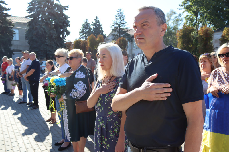 Міський голова Дмитро Зражевський разом із секретарем міської ради Оленою Заікою, жителями громади стоять на площі, долоні правих рук прикладені до сердець.