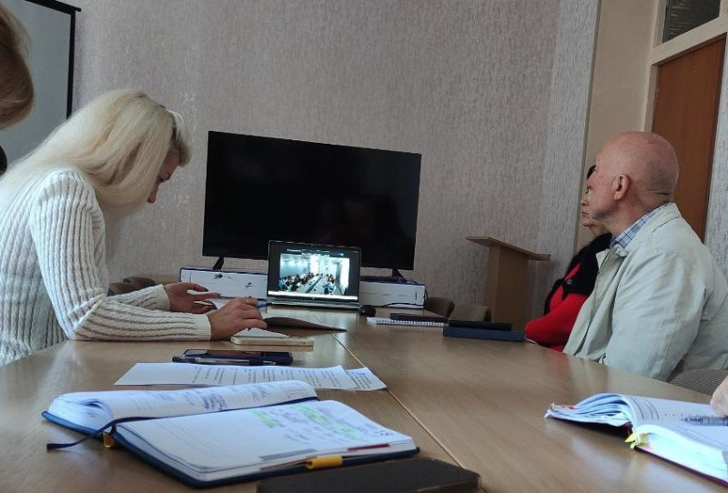 За столом сидять учасники засідання. Стоїть ноутбук. На екрані -  фрагмент засідання іншої групи людей. 