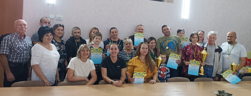 Спільне фото учасників змагань: діти, батьки, організатори. Усі усміхнені. У руках учасників - кубки, грамоти, на грудях - медалі.