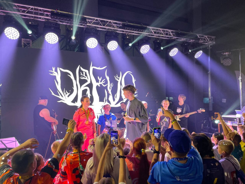 Члени команди на сцені зі співаком DREVO.  Сцену оточують інші учасники заходу, які фотографують співака.