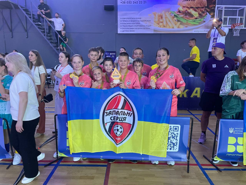 Спільне фото учасників команди з нагородами. У руках тримають Прапор України з емблемою команди. 