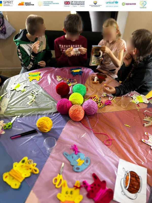 Хлопчики сидять за столиком, на якому лежать  ножиці, різнокольорові клубки ниток, поробки.