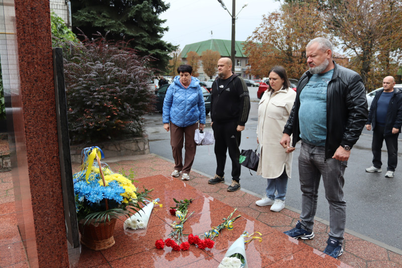 Представник районної влади, громадськості, соцслужби  стоять у підніжжя пам'ятного знаку, схиливши голови у хвилині мовчання. У  підніжжя знаку - квіти.