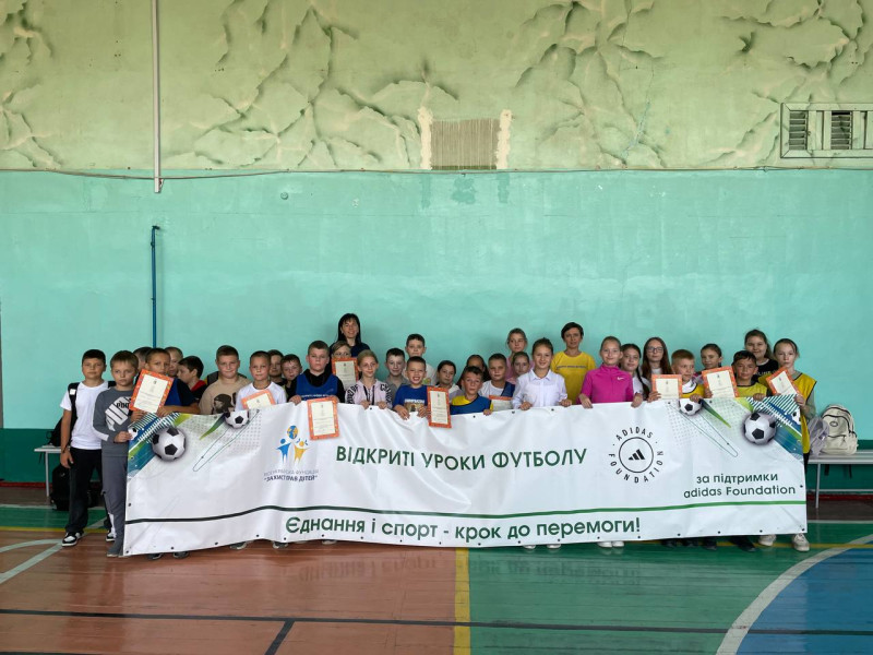 Діти разом із наставницями  у спортивній залі,  тримають грамоти  і  банер з написом: "Відкриті уроки футболу. Єднання і спорт - крок до перемоги".  